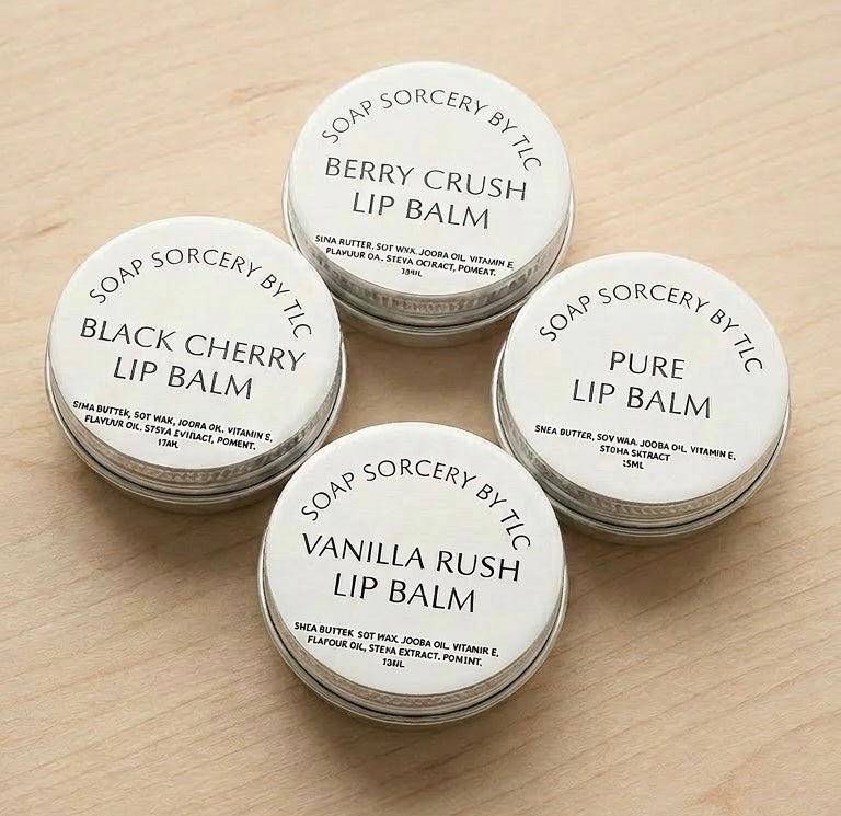 Four round metal tins of lip balm arranged on a light wood surface. The lids are white with black text reading 'SOAP SORCERY BY TIC' and the balm varieties: Berry Crush, Black Cherry, Pure, and Vanilla Rush.