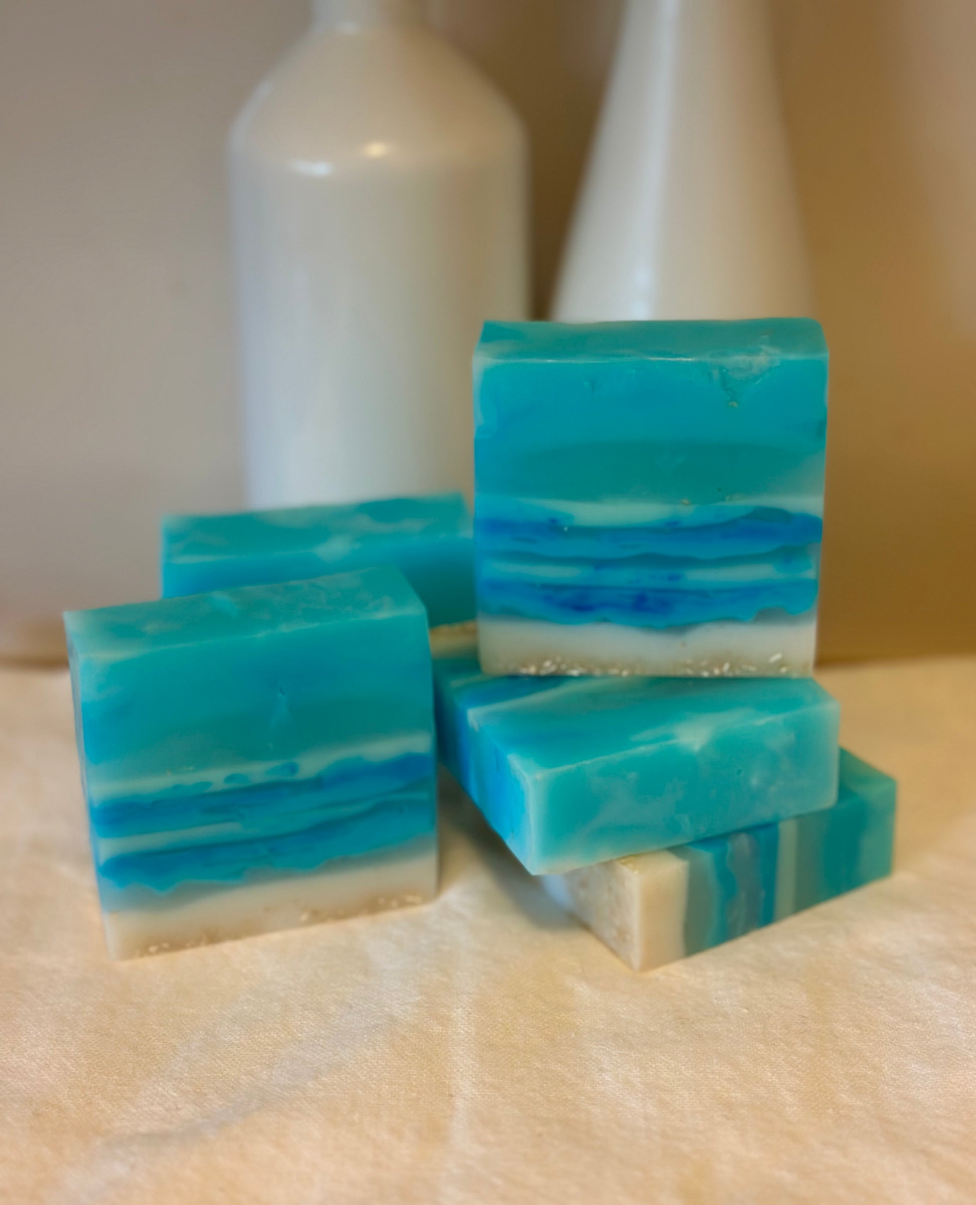 Stack of blue and white striped soap bars on a beige surface with two white bottles in the background.